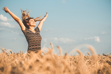 happy beautiful young woman enjoying nature, raising hands on background of cloudy sky in wheat...