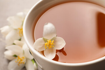Obraz na płótnie Canvas Cup of aromatic jasmine tea and fresh flowers, closeup
