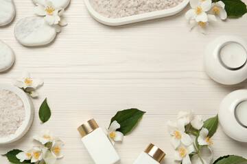 Fototapeta na wymiar Frame of beautiful jasmine flowers, spa stones and skin care products on white wooden table, flat lay. Space for text
