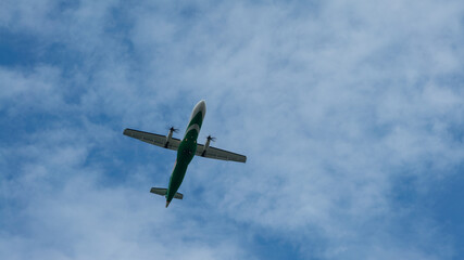 Fototapeta na wymiar View of propeller plane flying low with blue sky and clouds at background.