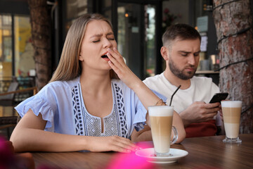 Young woman having boring date with guy in outdoor cafe