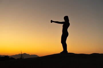 Silueta de chica haciendo técnica de boxeo, en la montaña a la hora del atardecer, con espacio...