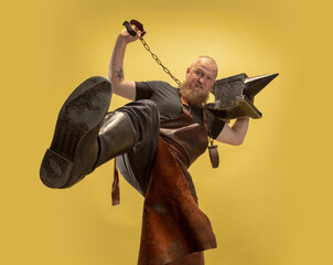 Bottom view of muscular bearded bald man, blacksmith in leather apron or uniform isolated on yellow...