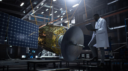 Industrial Engineer Working on Artificial Satellite Construction. Aerospace Agency: African American Scientist Using Tablet Computer to Develop Spacecraft for Space Exploration and Data Communication.