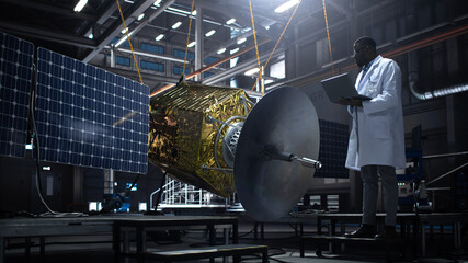 Industrial Engineer Working on Artificial Satellite Construction. Aerospace Agency: African American Scientist Using Tablet Computer to Develop Spacecraft for Space Exploration and Data Communication.
