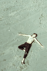 Half-naked guy lies on sandy beach. View from above