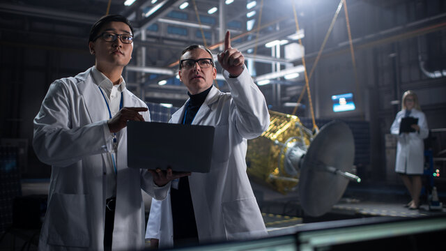 Engineer and Technician Working on Satellite Construction. Aerospace Agency: Diverse Team of Scientists Using Technological Equipment and Laptop Computer to Develop Spacecraft for Space Exploration.