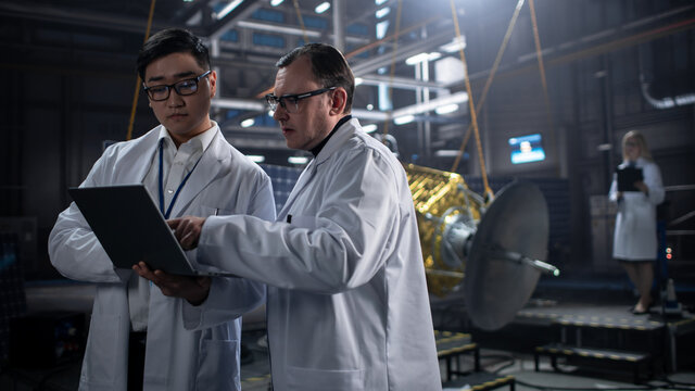 Engineer and Technician Working on Satellite Construction. Aerospace Agency: Diverse Team of Scientists Using Technological Equipment and Laptop Computer to Develop Spacecraft for Space Exploration.