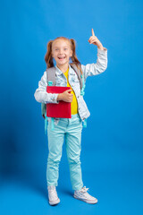 a little girl with a backpack holds a book on a blue background
