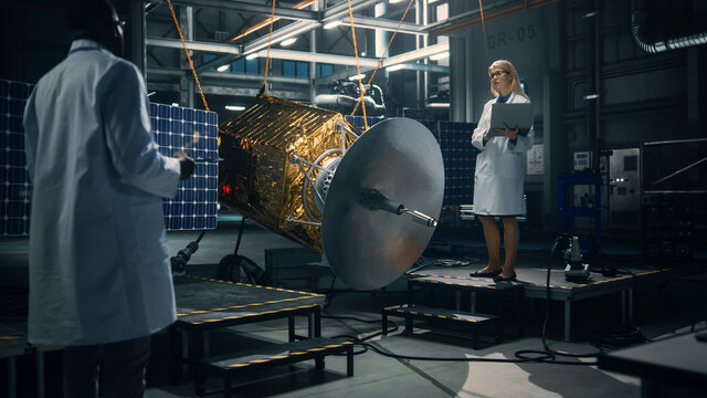 Engineer and Technician Working on Satellite Construction. Aerospace Agency: Diverse Team of Scientists Using Technological Equipment and Laptop Computer to Develop Spacecraft for Space Exploration.
