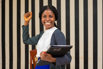 Single happy young executive with long brown hair and black jacket standing in small office holding...