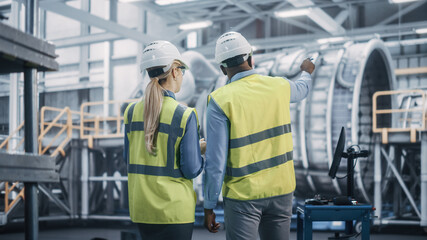 Two Diverse Professional Heavy Industry Engineers Wearing Safety Uniform and Hard Hats Working on...
