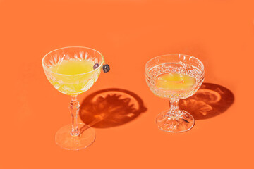 Two luxurious crystal glasses with yellow cocktails against orange background.One glass have two chokeberries on top of it.