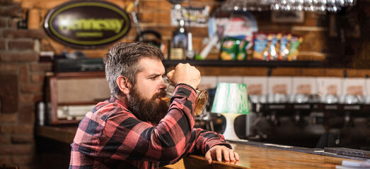 Man drinks beers at the bar counter. People, lifestyle, recreation. Man with beer. Bearded hipster holds glass of beer. Beer pub. Stylish guy at cafe pub. Beer time