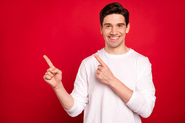 Photo of funny brunet millennial guy point empty space wear white shirt isolated on red color...