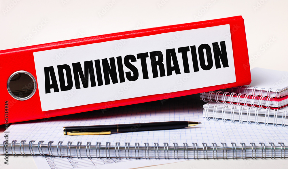 Poster on the desktop are notebooks, a pen and a red folder for papers with the text administration. busine
