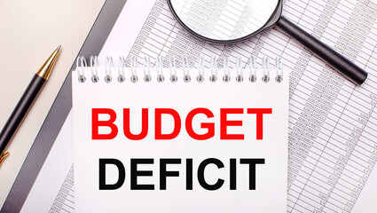 Desktop magnifier, reports, pen and notebook with text BUDGET DEFICIT. Business concept