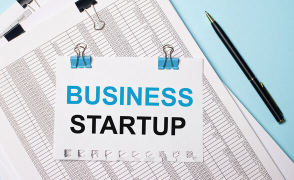 On a light blue background, documents, a pen and a sheet of paper on blue paper clips with the text BUSINESS STARTUP. Business concept.