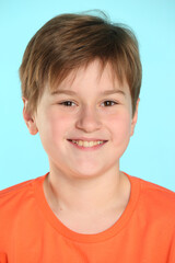 Close-up portrait: a handsome developed cheerful teenage boy in an orange T-shirt smiles and looks eye to eye.
