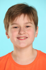 Close-up portrait: a handsome developed cheerful teenage boy in an orange T-shirt smiles and looks eye to eye.