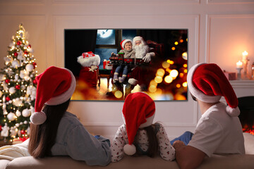 Family watching TV movie in room decorated for Christmas, back view - obrazy, fototapety, plakaty