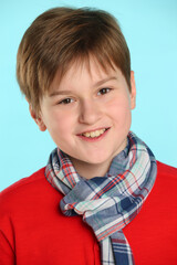 Close-up portrait: fashionable, cheerful teenage boy in a red sweater and a checkered scarf. He smiles and looks eye to eye.