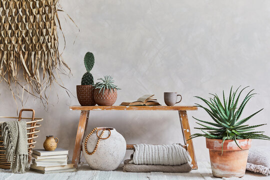 Stylish composition of cozy living room interior with copy space, bench in retro style, clay vase, crockery, straw wall decoration and textiles. Rustic inspiration. Summer vibes. Beige wall. Template.