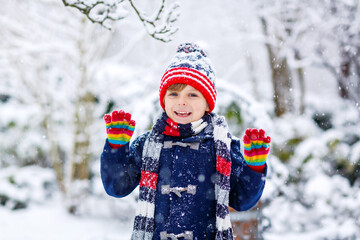 Funny little kid boy in colorful clothes playing outdoors during strong snowfall