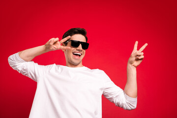 Fototapeta premium Photo portrait brunet guy in casual outfit wearing sunglass dancing at party showing v-sign isolated vibrant red color background