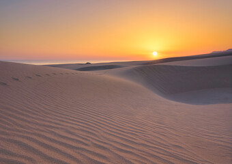 The sand dunes during sunset. Sun glow and dunes. Summer landscape in the desert. Hot weather. Lines in the sand. Landscape without people.