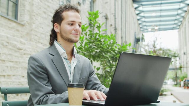 Young successful caucasian businessman works in an outdoor cafe using a computer and a smartphone. Business, freelance and remote work.