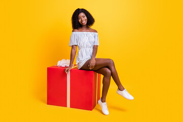 Portrait of attractive cheerful girl sitting on big giftbox festal occasion isolated over bright...