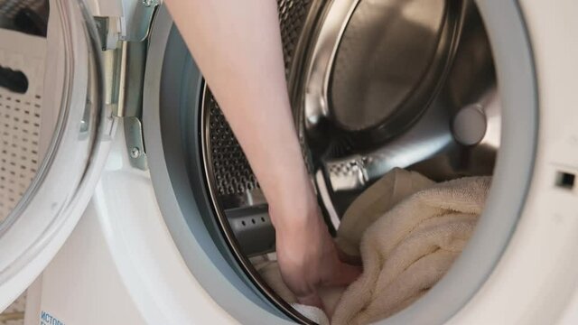 Washing machine laundry. Housewife hands load automatic machine with white terry towels and close door under electric light in home bathroom macro