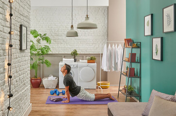 Man is doing sport at home, living room and laundry room, frame, lamp, bookshelf and green plant.