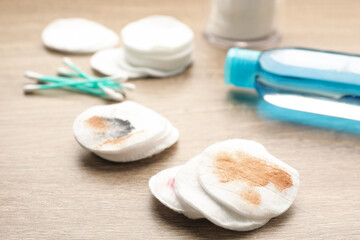 Dirty cotton pads and makeup removal product on wooden table, closeup