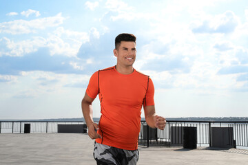 Handsome man in sportswear running outdoors on sunny day