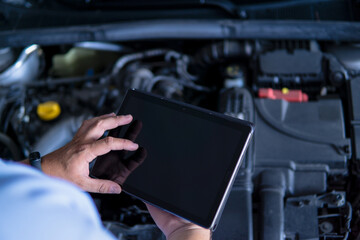 Auto mechanic with digital tablet at work making an engine repair diagnosis of a car in a mechanic garage
