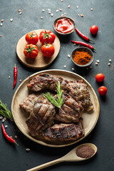 Pieces of grilled carp on a round plate, tomatoes, peppers, spices on a dark background. 