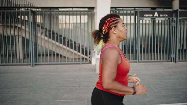 Cardio workout. Chubby african american woman practicing jog training outdoors, running alone in evening city, back view