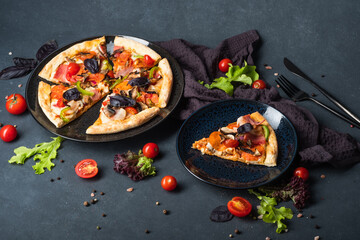 Savory Homemade Meat Pizza with Pepperoni, Bacon, tomatoes and basil on a dark background.