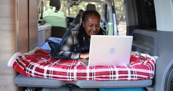 Mature african woman using computer laptop inside mini van camper - Elderly person on a road trip vacation
