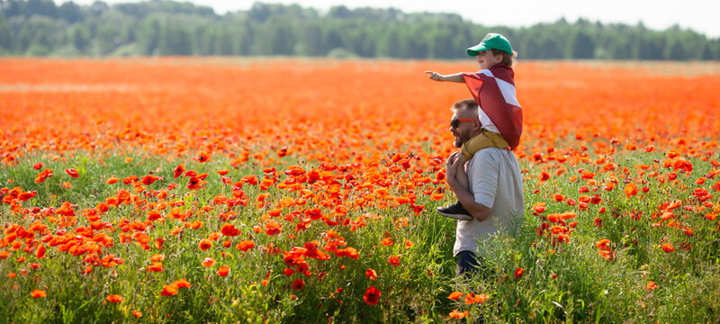 Dad holding his little son covered with flag of Latvia on his shoulders in the poppy field. Declaration of Independence Day. Ligo. Proclamation of the Republic. Travel, learn latvian language concept.