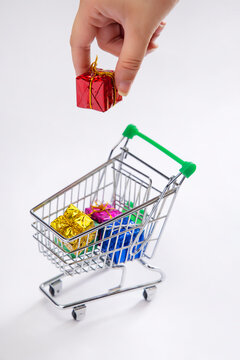 A human hand putting a gift box in a shoppingcart of presents.