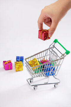 A human hand putting a gift box in a shoppingcart of presents with gift boxes kept alongside.
