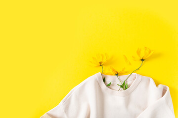 Autumn shopping, discount and sale concept. Knitted sweater and autumn flowers on a bright yellow background. Flat lay, copy space. Fall promotion. Clothes care, dry cleaning, ecological production