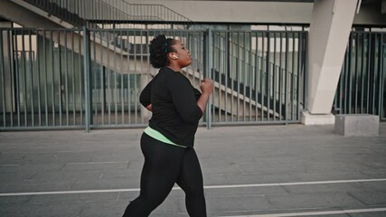 Slimming concept. Young overweight african american woman training alone, running and listening to music in earphones