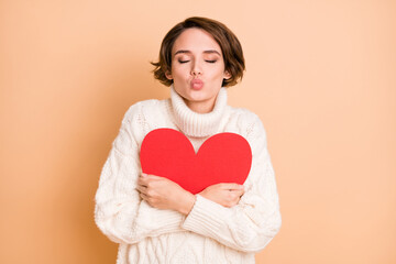 Photo of lovely charming young woman hug red paper heart send air kiss isolated on beige color background