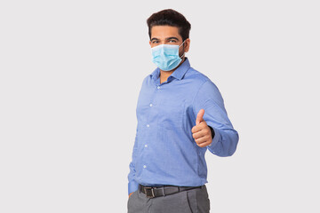 Portrait of a man showing thumbs up with mask on face against plain background.