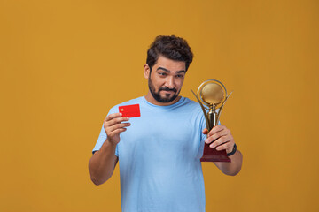 Portrait of a man holding a credit card and trophy against plain background.