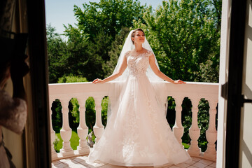 the bride in a white lace dress and a long veil stands on the terrace.